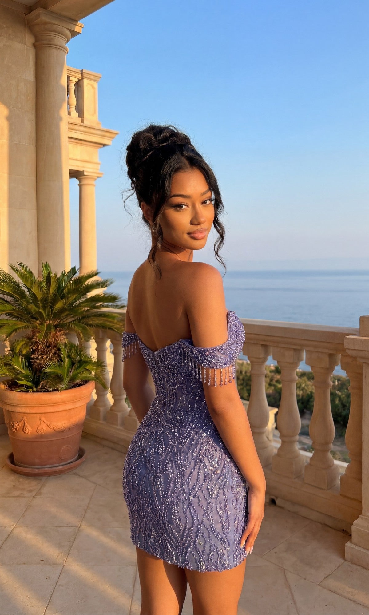 A woman in the Beaded Glitter Hoco Dress: PromGirl Exclusive 250133 with off-the-shoulder sequined sleeves stands on a balcony with columns, overlooking water and greenery under a clear sky.